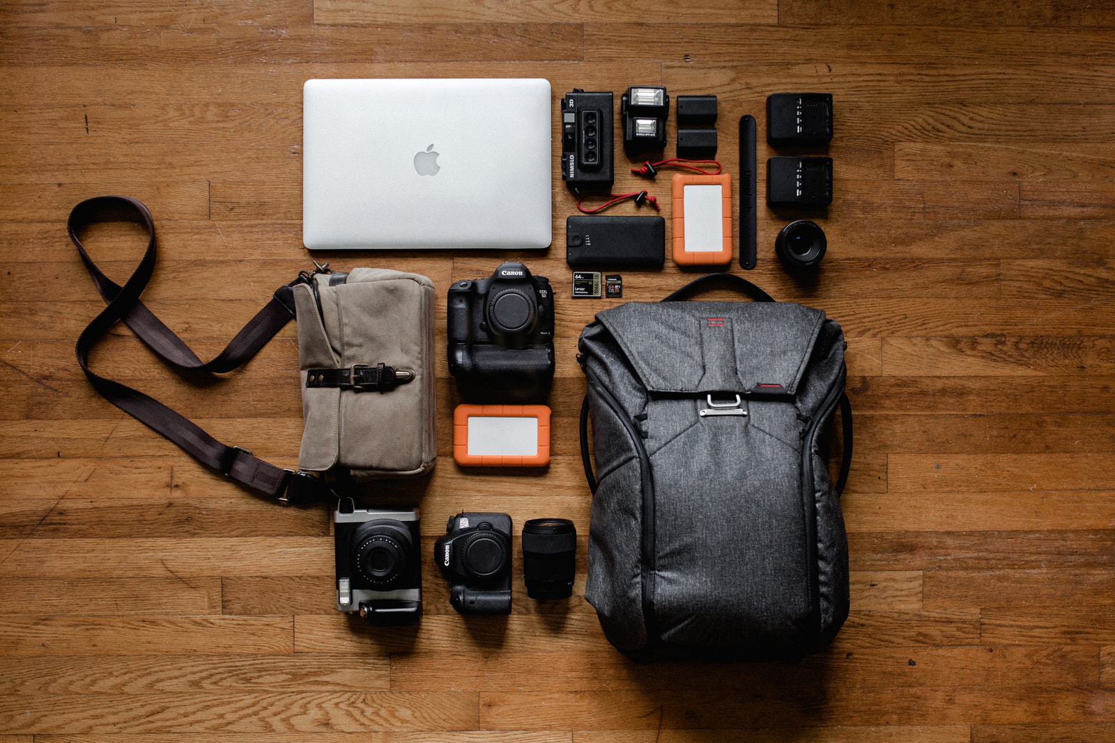Photography business equipment including camera bag, camera lenses, hard drives, computers on a wood table