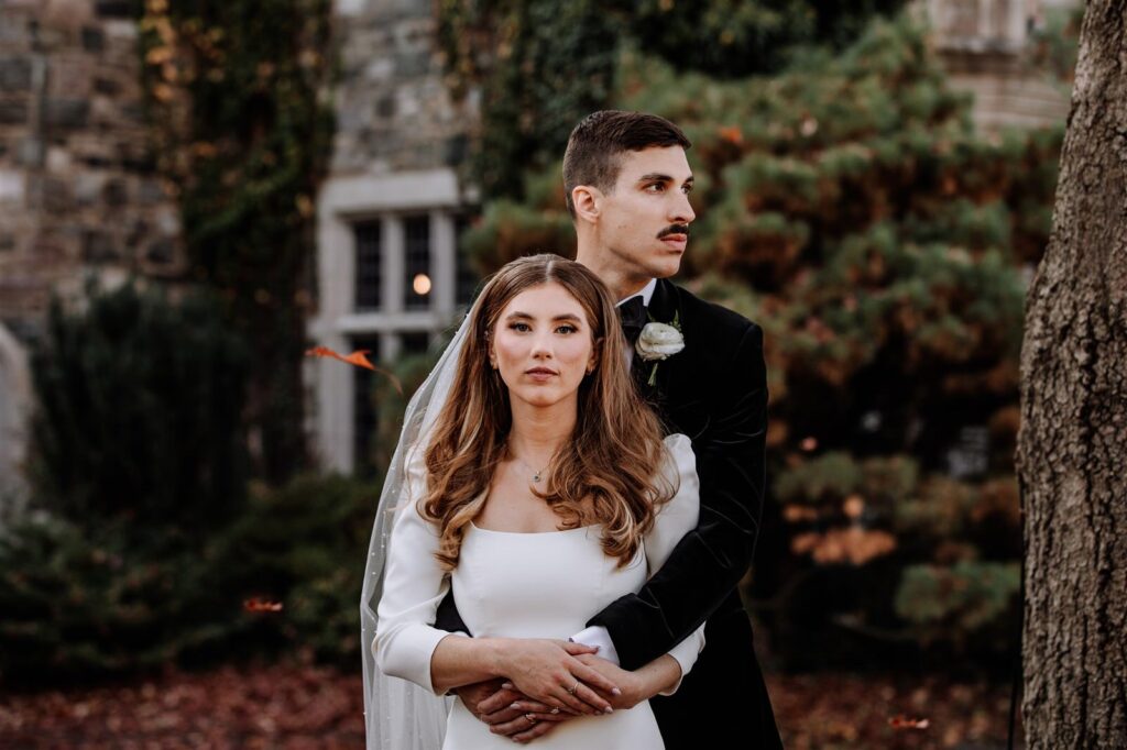 couple in wedding attire looking towards the camera while a leaf falls from a tree