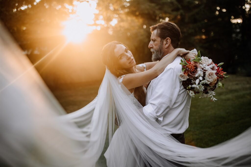 newly married couple portrait with sun glare in background and brides veil in foreground