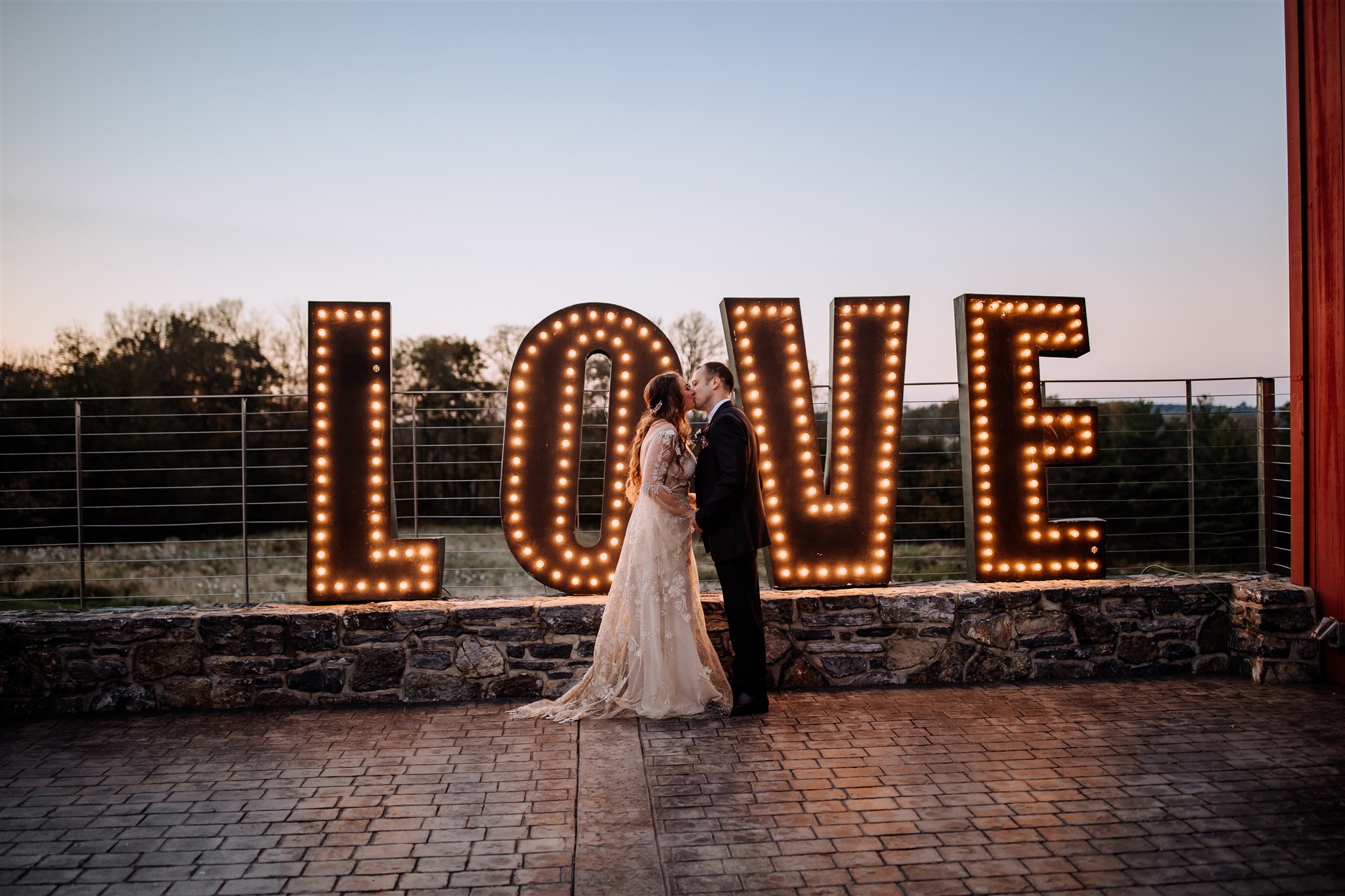 bride and groom standing in front of a LOVE sign during sunset