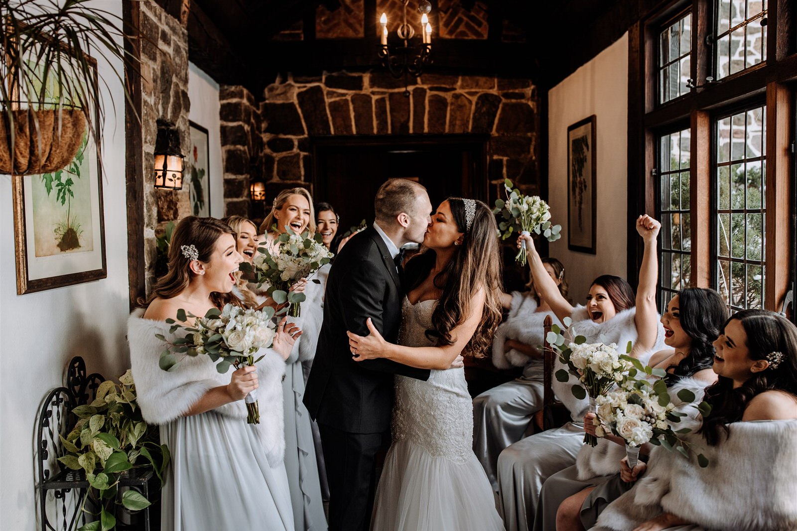 Bride and groom kissing with bridal party around them and cheering