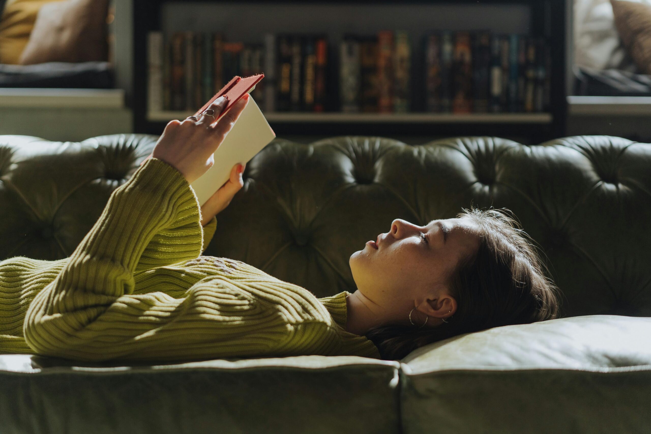 Girl reading a book while laying down on the couch